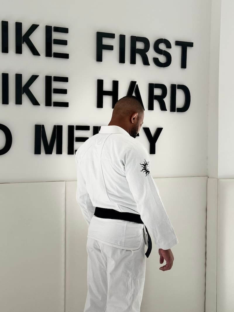 Person wearing BLITZ Sun & Moon BJJ Gi with black belt, standing against wall with inspirational text.