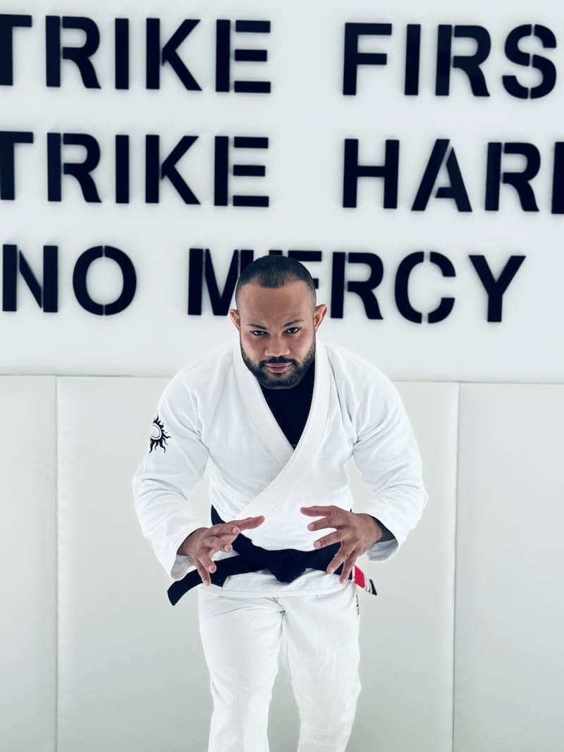 BJJ practitioner in BLITZ Sun & Moon Unisex Gi demonstrates stance in front of motivational wall text.