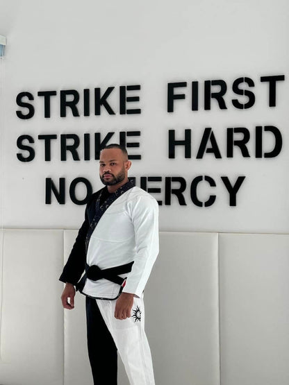 Unisex Brazilian Jiu-Jitsu Gi Model Posing in Front of "Strike First, Strike Hard, No Mercy" Wall Sign