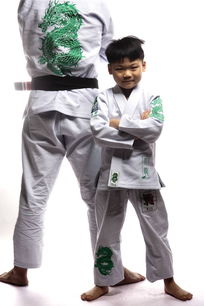 Child in ZHAN Year of the Dragon Limited Edition BJJ Gi with green dragon embroidery, standing confidently next to an adult in matching gear.