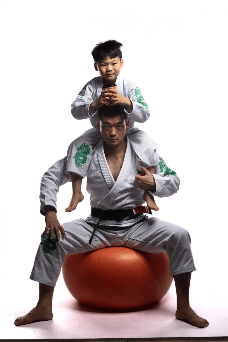 Adult and child wearing ZHAN Year of the Dragon Limited Edition BJJ Gi practicing together on an exercise ball