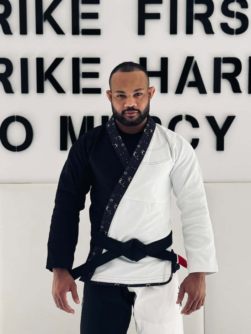 Man wearing BLITZ Sun & Moon Brazilian Jiu-Jitsu Gi, combining durability and style, against motivational wall.