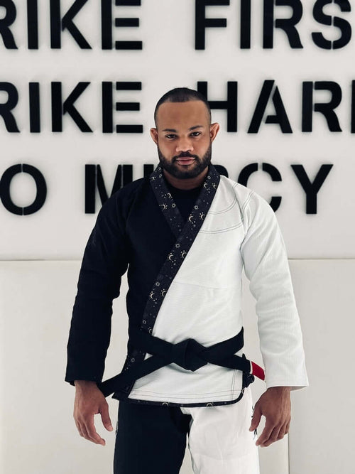 Man wearing BLITZ Sun & Moon Brazilian Jiu-Jitsu Gi, combining durability and style, against motivational wall.