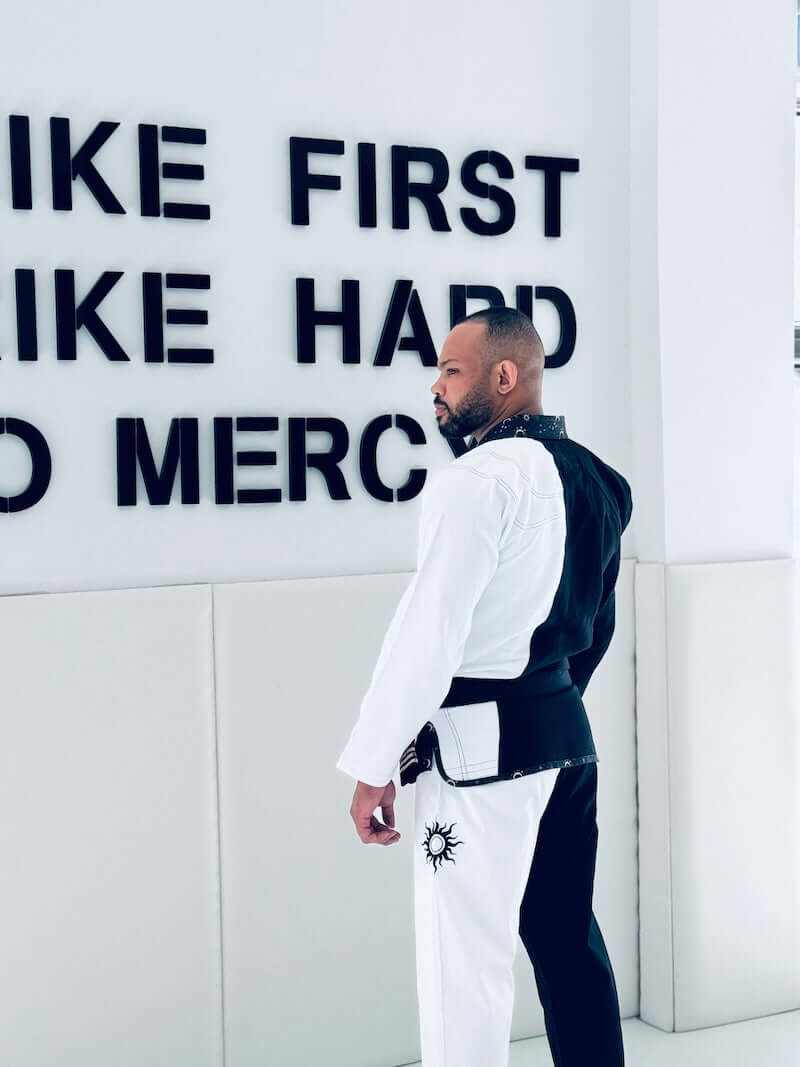 BLITZ Sun & Moon Brazilian Jiu-Jitsu Gi worn by a practitioner facing a motivational wall in a training setting.