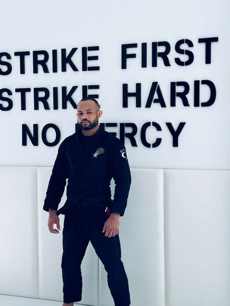 A practitioner wearing the BLITZ Sun & Moon Brazilian Jiu-Jitsu Gi poses confidently against a motivational wall.