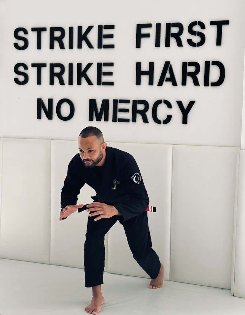 A practitioner wearing the BLITZ Sun & Moon Brazilian Jiu-Jitsu Gi in a training setting with motivational wall text.
