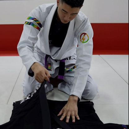 Model in a white rainbow pattern BJJ gi folding the gi